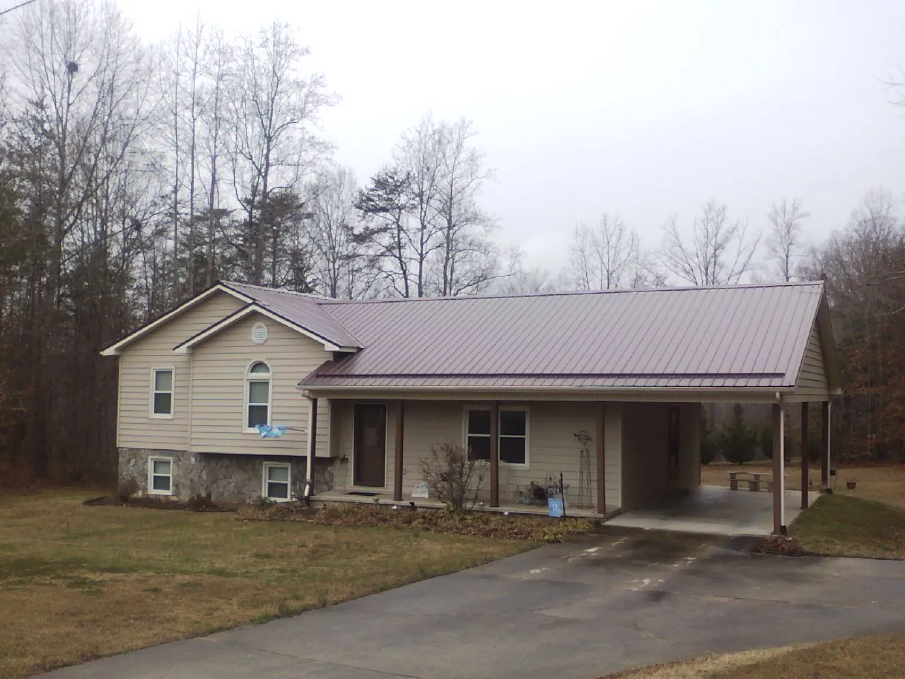 Burgundy metal roof on a tan split level home with an attached carport in Waynesville