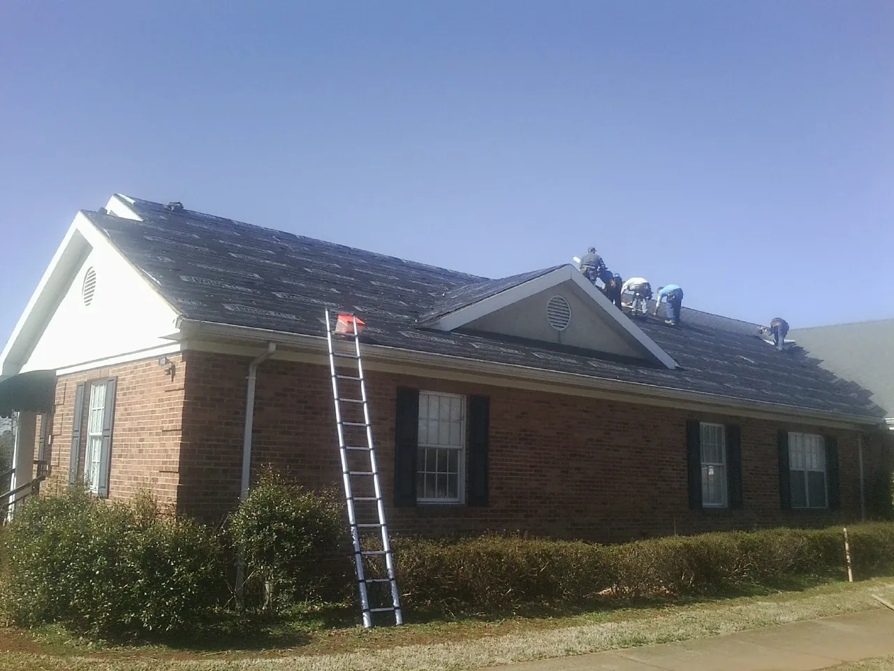 Crew tearing shingles off a brick ranch roof with a ladder set — Metal Roof Repair work by our crew in Waynesville