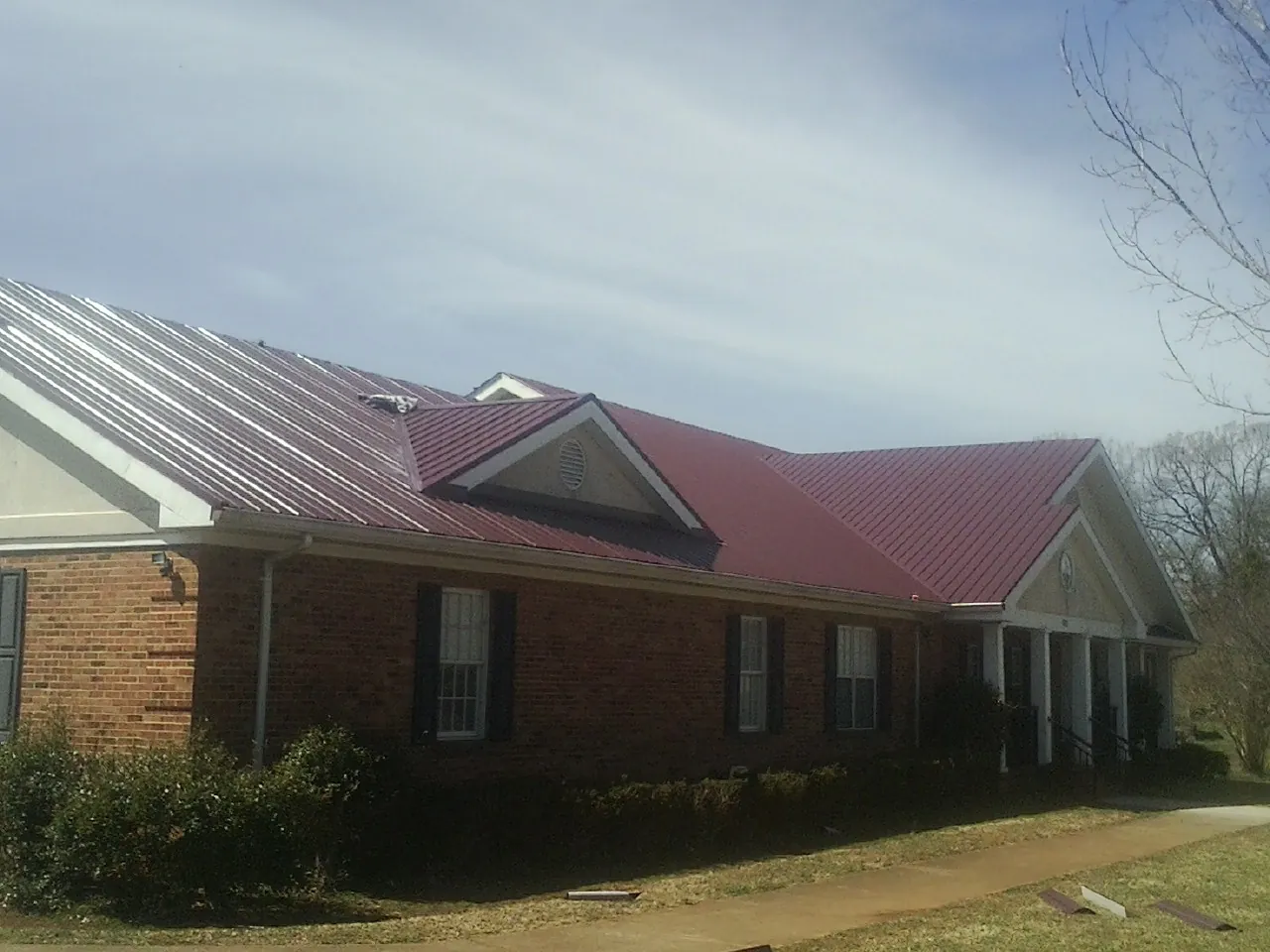 Red metal roof with gabled entries on a long brick building, from a Hail Damage Roof Repair job in Waynesville
