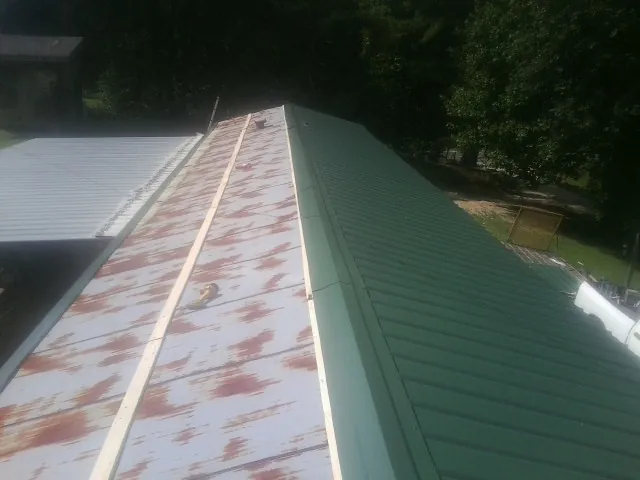 Old rusted panels beside newly installed green metal roofing — Wind Damage Roof Repair by Roofing Brothers in Waynesville